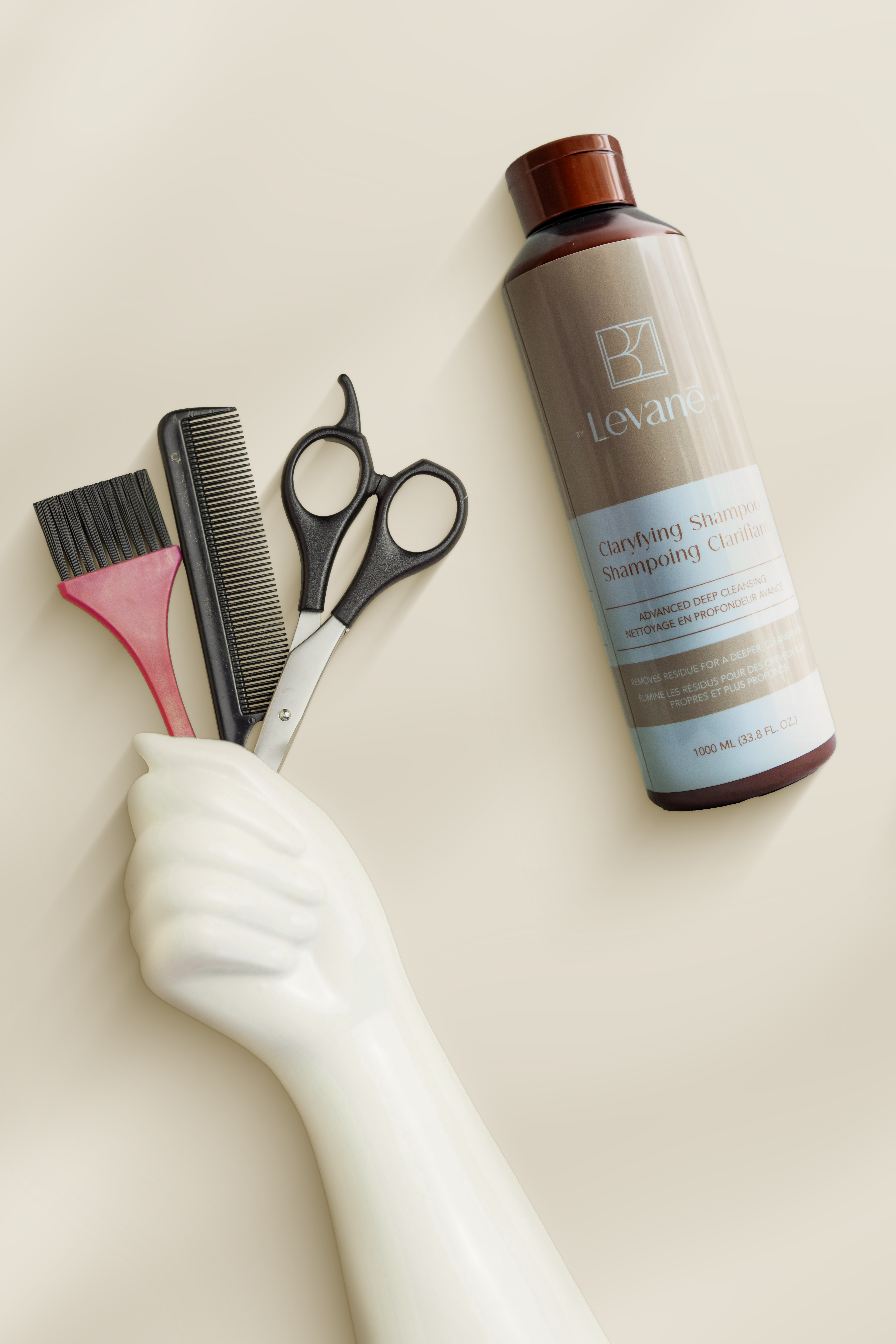 Shampoo bottle, brush, comb, and scissors on a beige background