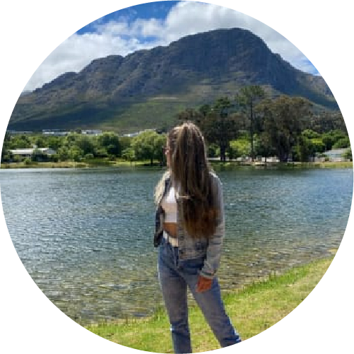 Person standing by a lake with mountains in the background